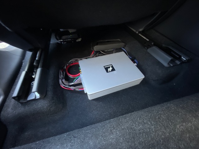 シートを最前にしてマットをめくるとμ-DimensionのプロセッサーアンプDSP680AMP V2が見えます。<br>内蔵6chアンプでフロント3Wayマルチ接続にし、プリアウトにてアンプ内蔵ウーファーを接続してプロセッサーコントロールしています。<br>ちなみにリアスピーカーはそのまま純正アンプで鳴りますのでディスプレイオーディオのフェダーコントロールを使用して家族でお乗りになる際は音を出したり、前席で聴くときはお好みで消したりする事が可能です。<br>